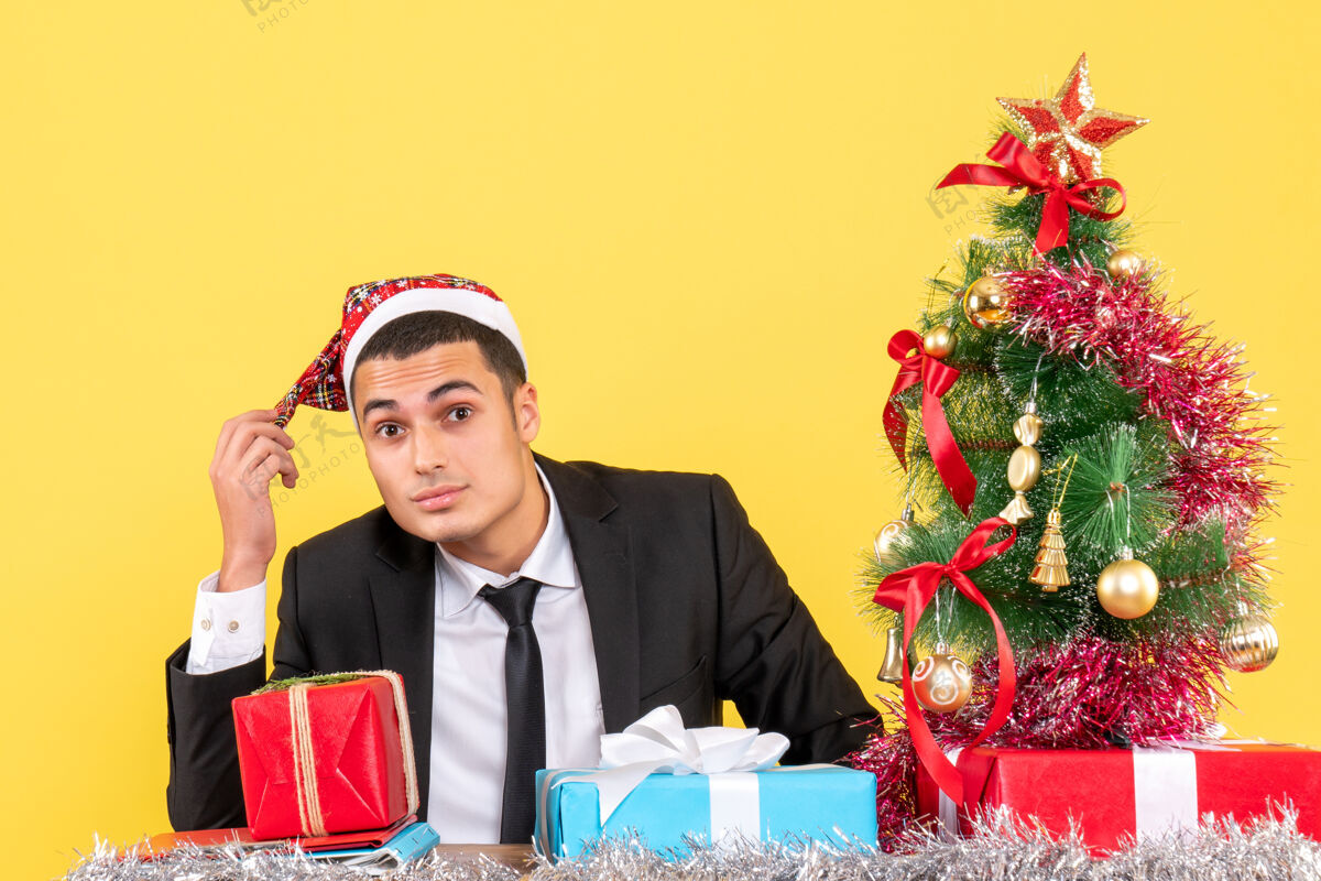 西装前视图穿着西装的人戴着圣诞帽坐在桌子旁圣诞树和礼物圣诞树圣诞节行政人员