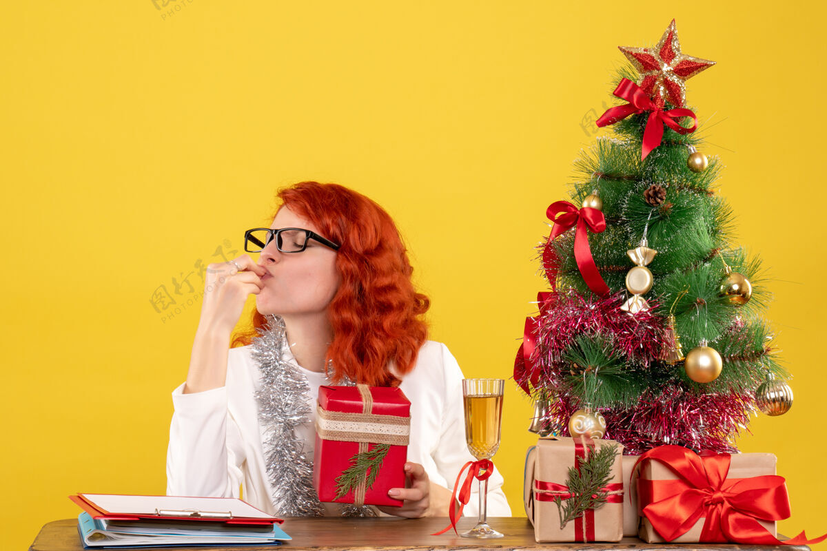 鲜花前视图：女医生坐在桌子后面 黄色背景上有圣诞礼物美丽礼物情感