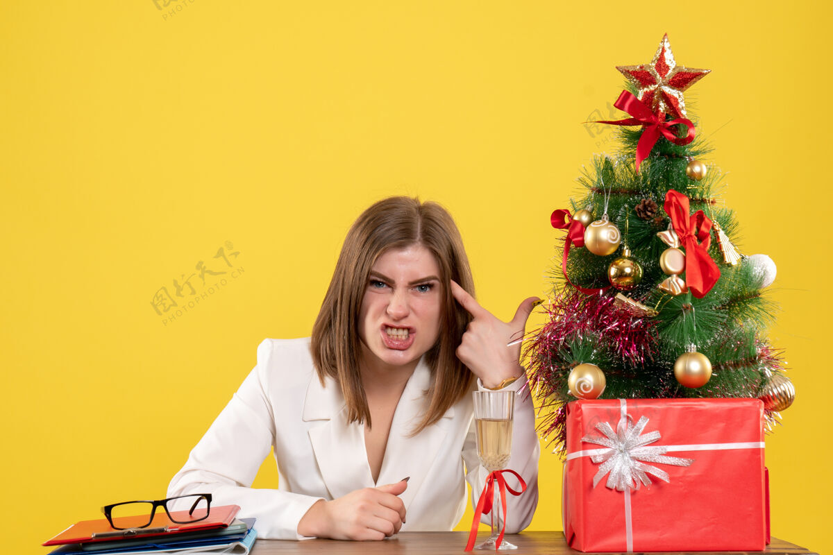桌子前视图：女医生坐在黄色地板上的桌子前 手里拿着圣诞树和礼品盒成人女人漂亮