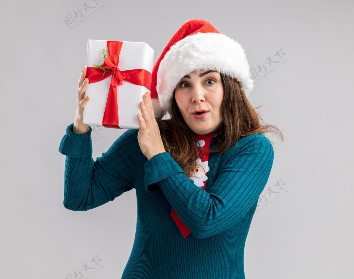 印象深刻印象深刻的成年白人妇女与圣诞帽和圣诞领带举行圣诞礼品盒隔离在白色背景与复制空间礼物圣诞节举行