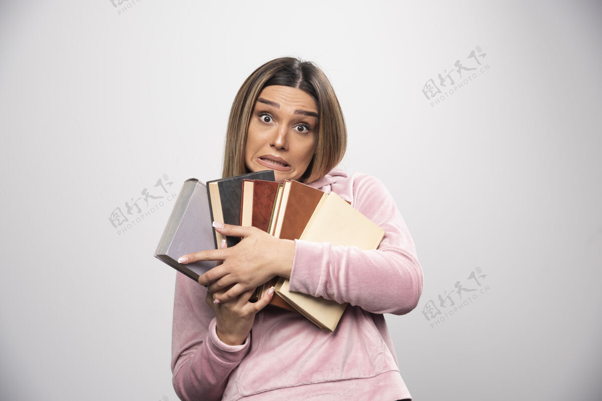 股票穿着粉红色衬衫的女孩手里拿着一大堆书女性姿势休闲