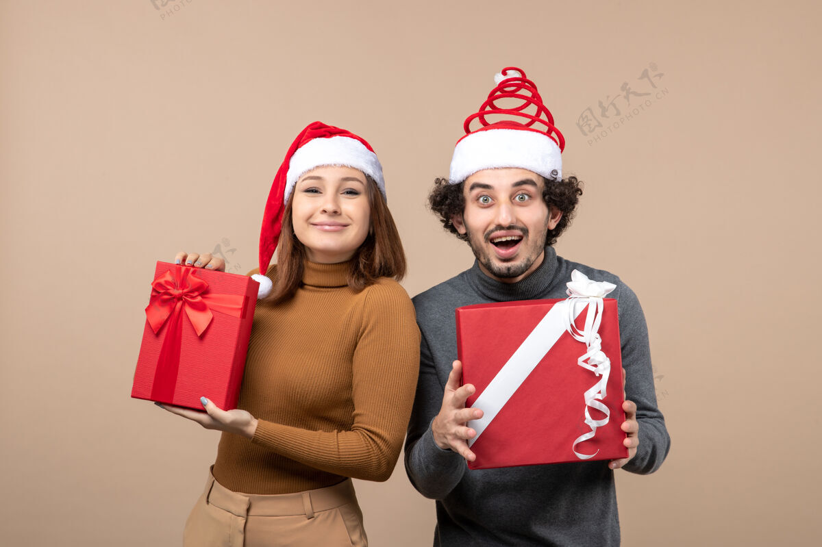 派对新年心情和派对理念-年轻快乐兴奋的可爱情侣手持礼物戴着圣诞老人的灰色帽子情侣帽子礼物