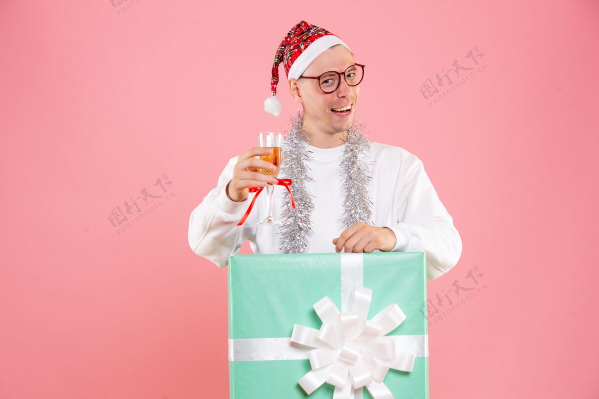 快乐粉红色墙上的年轻人拿着圣诞花环喝酒的正面图圣诞快乐花环节日