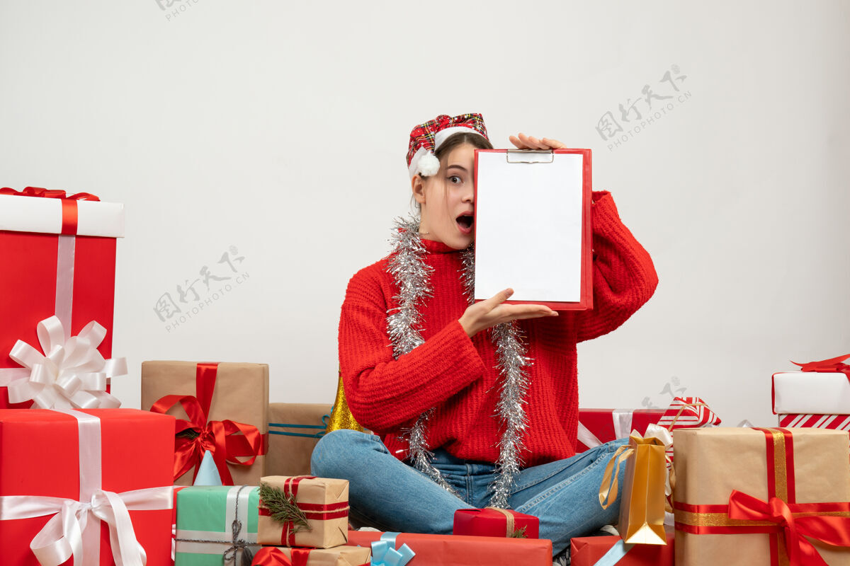 礼物惊讶的女孩戴着圣诞帽 用文件遮住眼睛 围坐在白色的礼物旁边文件高兴惊讶的女孩