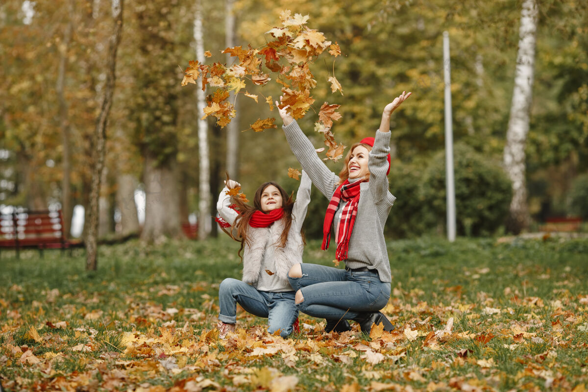 秋天时髦的母亲带着女儿黄色的秋天戴着红领巾的女人父母微笑叶子