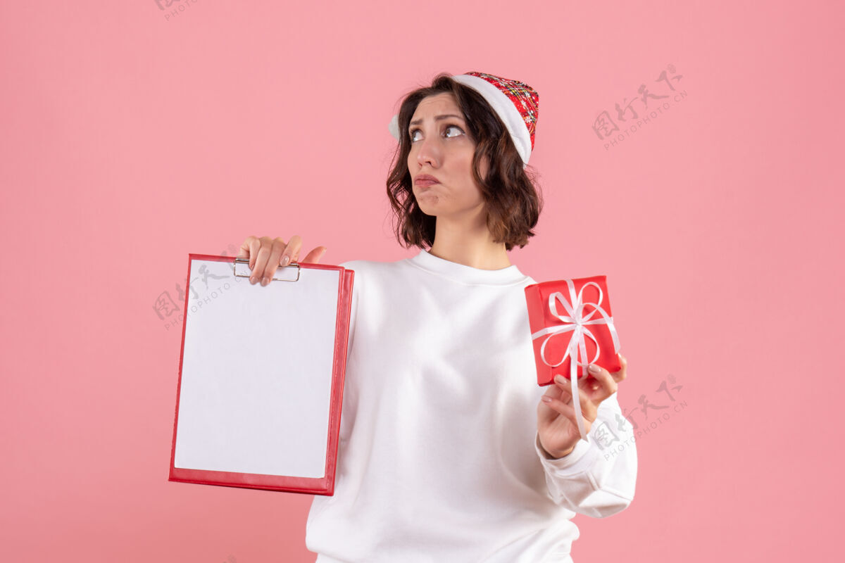 前面前视图的年轻女子举行小圣诞礼物和文件说明在粉红色的墙上文件女人圣诞节