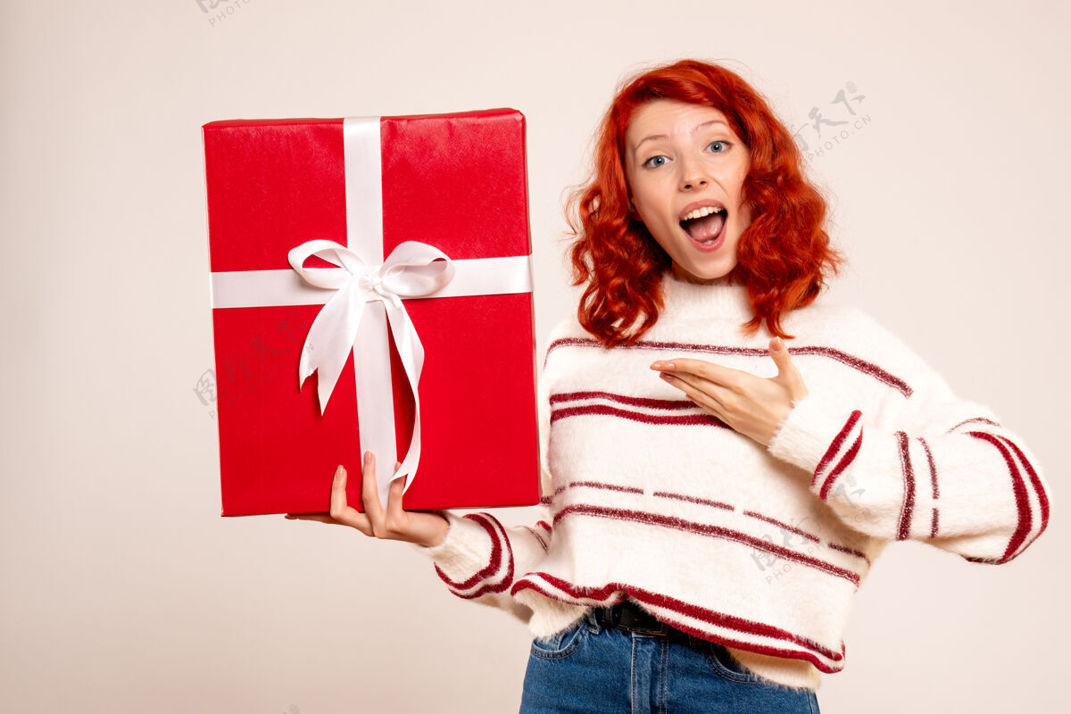 模特白墙上拿着大礼物的年轻女子的正面图十二月节日礼物