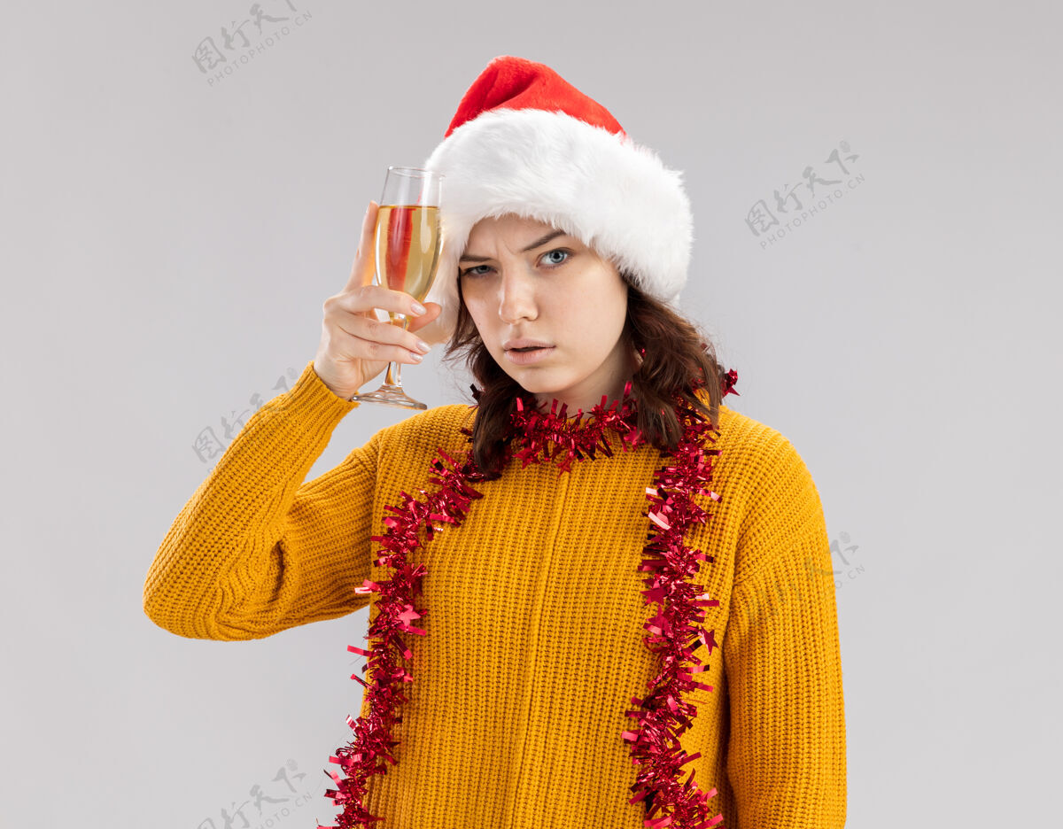 圣诞快乐自信的年轻斯拉夫女孩 戴着圣诞帽 脖子上戴着花环 手里拿着一杯香槟 背景是白色的 有复制空间花环年轻自信