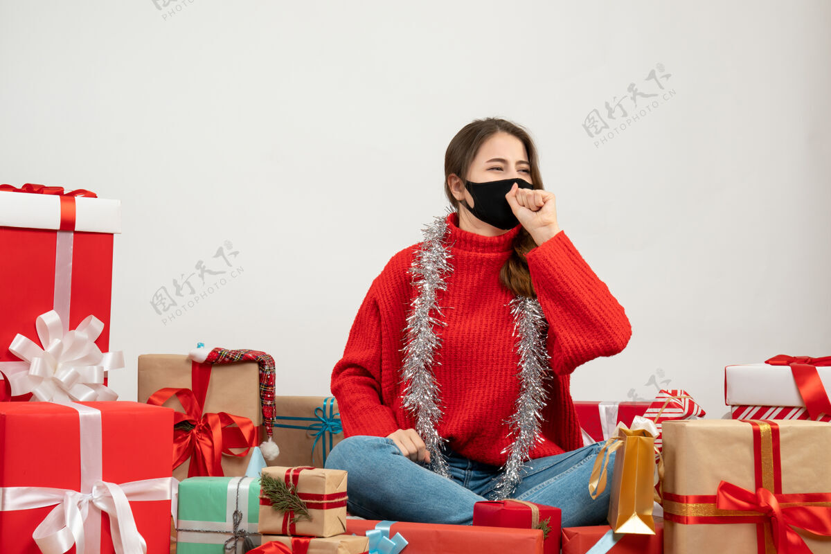 漂亮穿着红色毛衣的年轻女孩看着右边围坐着的礼物 白色的面具上戴着黑色的面具红色黑色毛衣