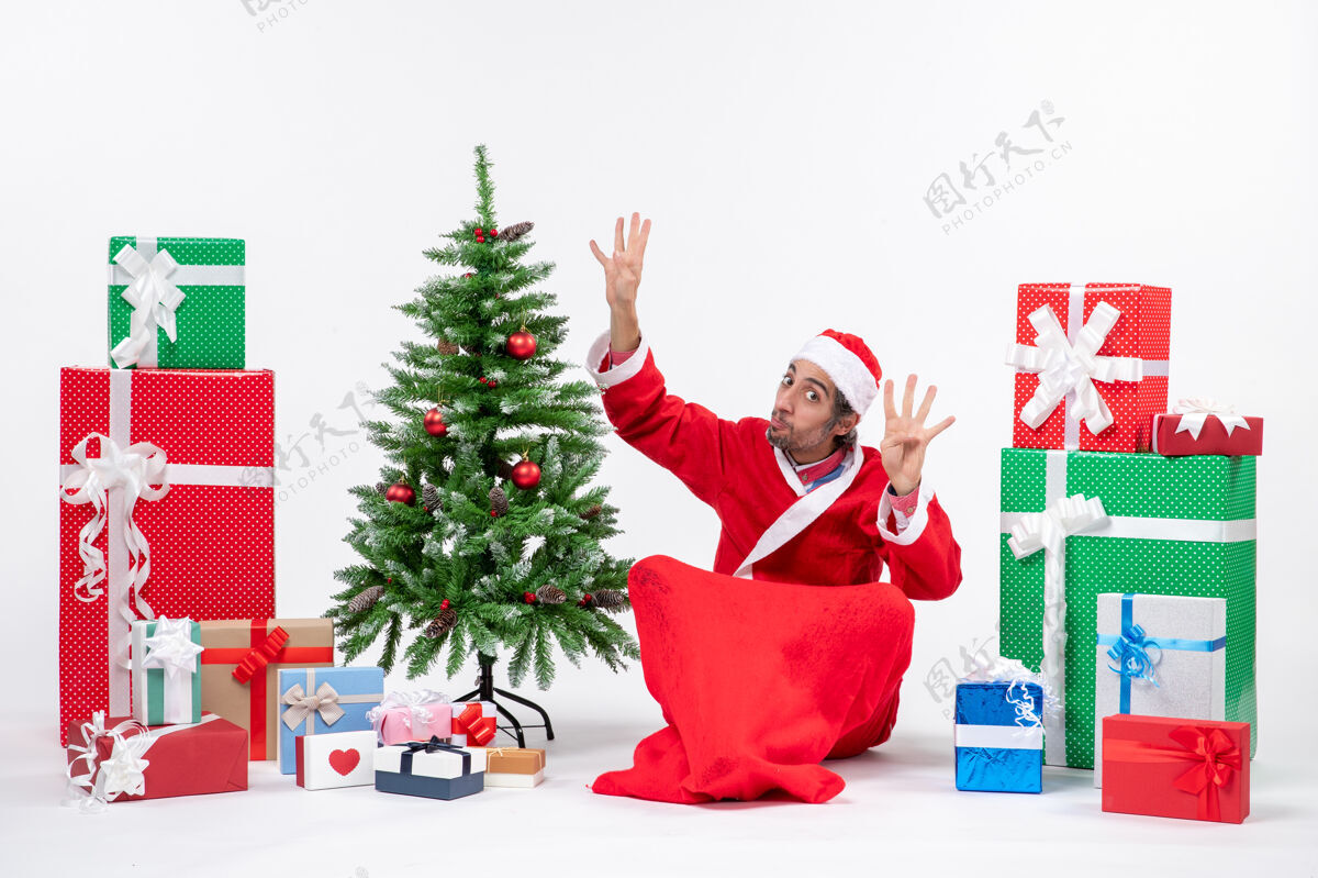 圣诞年轻的成年人打扮成圣诞老人 拿着礼物和装饰好的圣诞树坐在地上展示着八个八圣诞树礼物