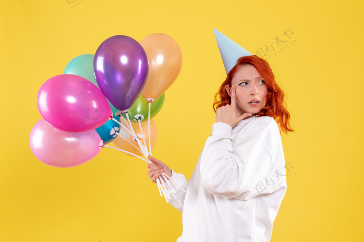 女性黄色墙壁上手持彩色气球的年轻女子的正视图快乐举行乐趣