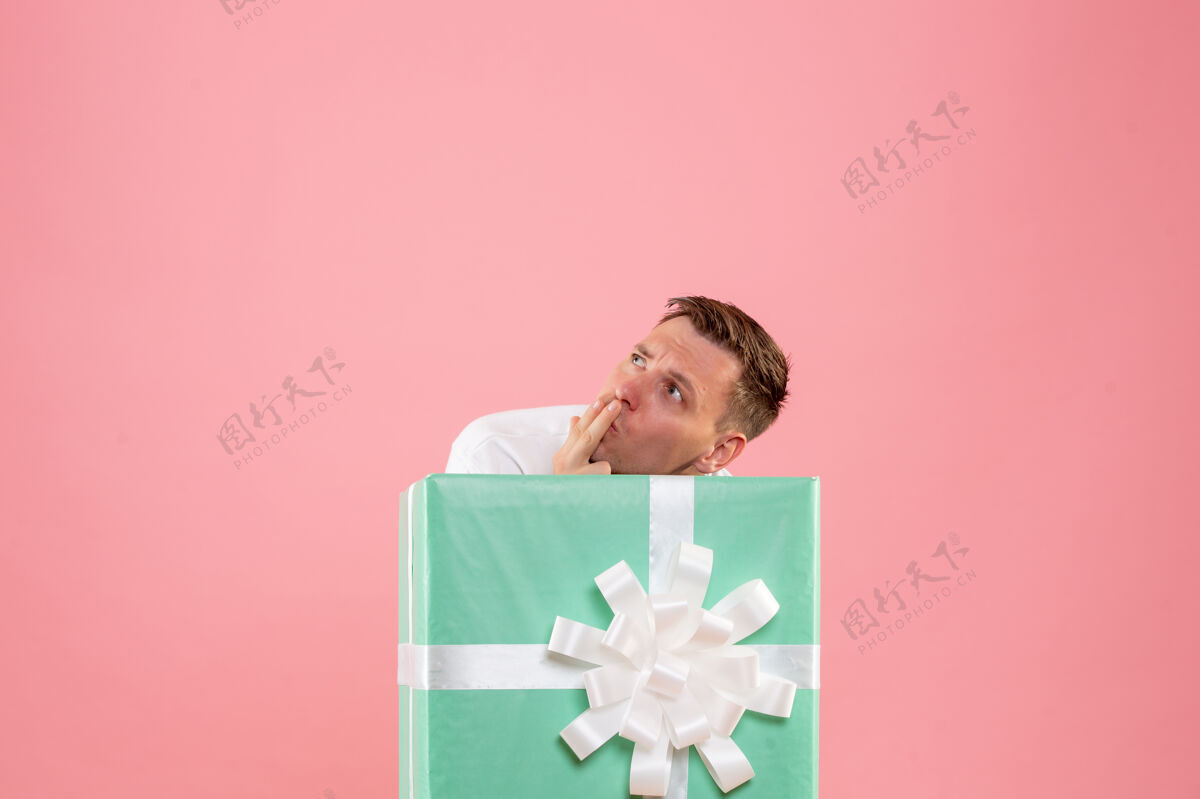 人隐藏在粉红色墙上的礼物里面的年轻人的正面视图脸情感十二月