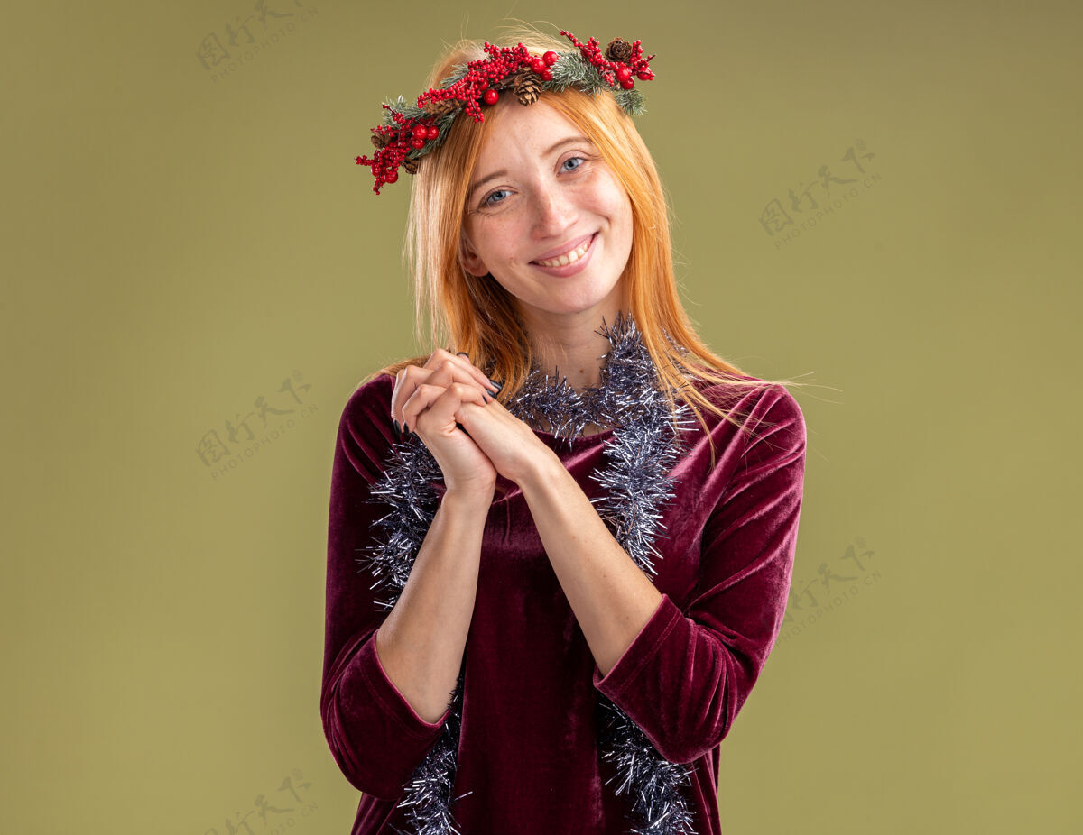 年轻微笑着的年轻漂亮的女孩穿着红色的裙子 脖子上戴着花环和花环 手牵着手 在橄榄绿的背景下与世隔绝女孩微笑一起