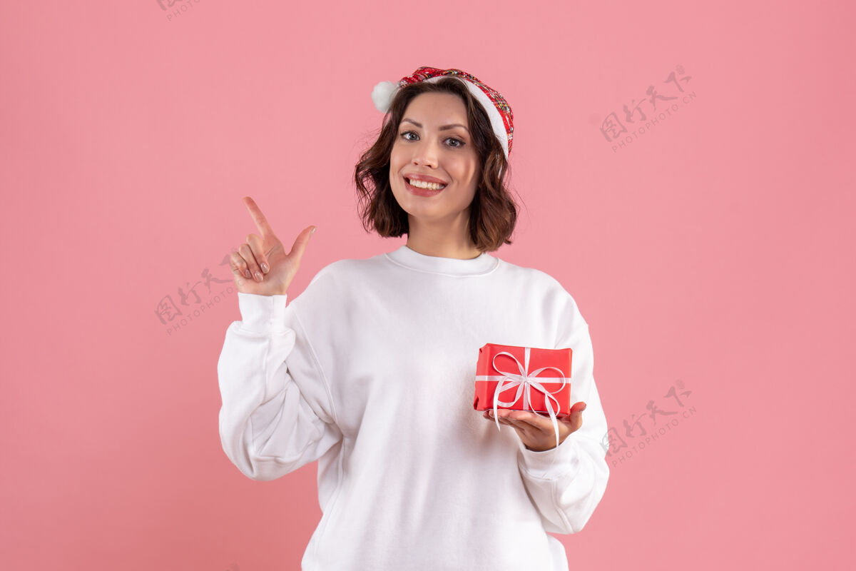 情感前视图的年轻女子举行小圣诞礼物在粉红色的墙上肖像圣诞节球衣