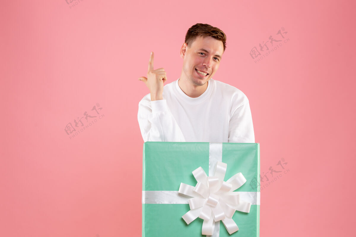 快乐隐藏在礼物里的年轻人在粉红色墙上微笑的正面视图肖像礼物成人
