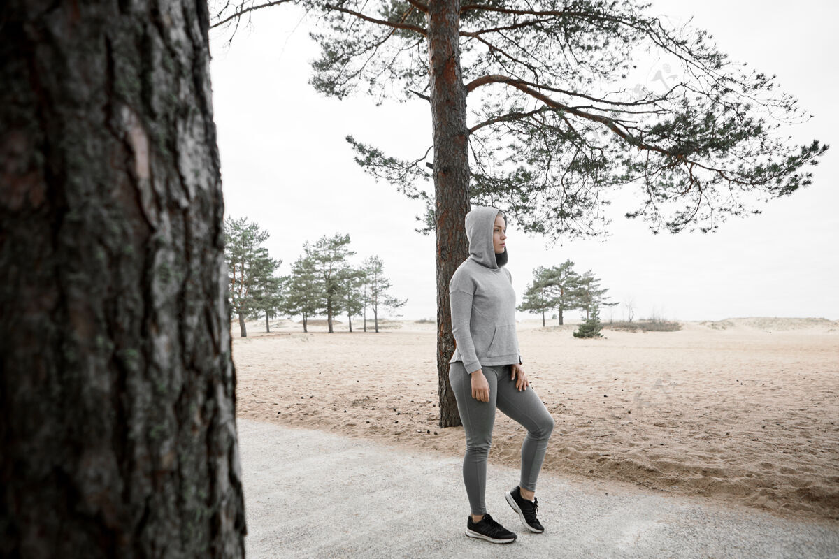 锻炼酷酷时尚的欧洲女跑步者在户外有氧训练前热身的全长镜头 穿着时尚的运动鞋 紧身裤和连帽衫 站在森林或公园里铺好的小路上女孩运动鞋马拉松