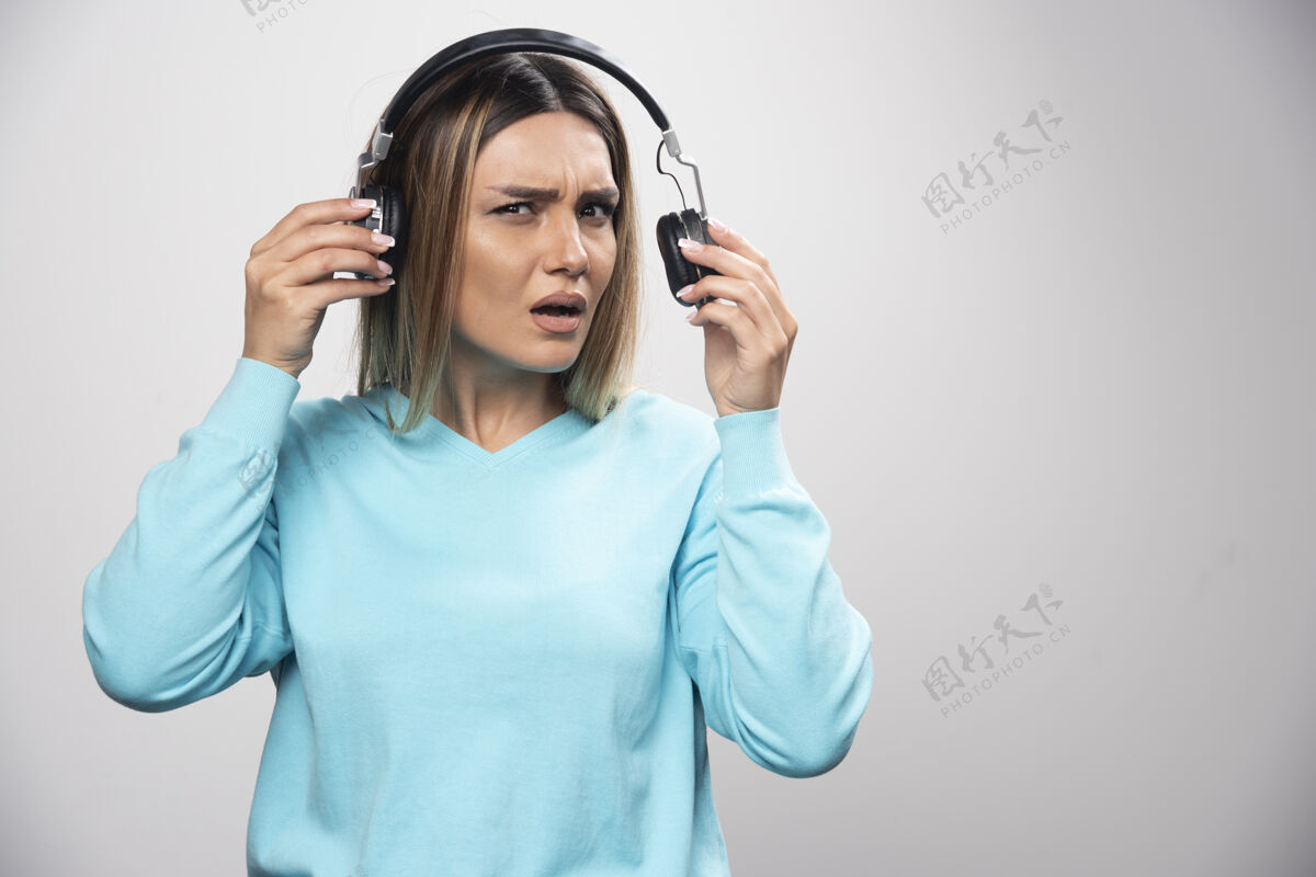 音乐穿着蓝色运动衫的金发女孩听着耳机 却不喜欢音乐女不同意人