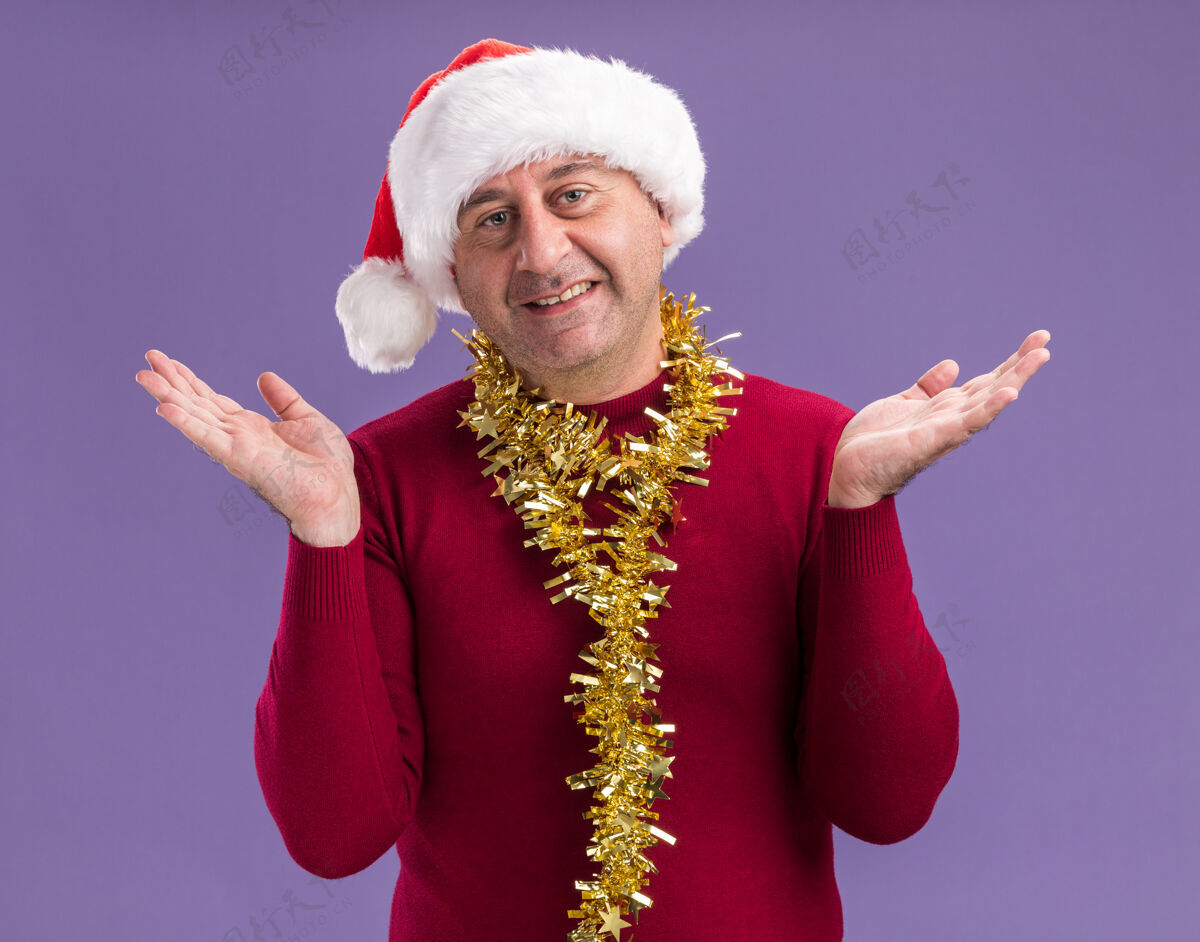 中间中年男子戴着圣诞老人帽 脖子上戴着金属丝 站在紫色的背景上微笑着看着摄像机站立圣诞老人金属片