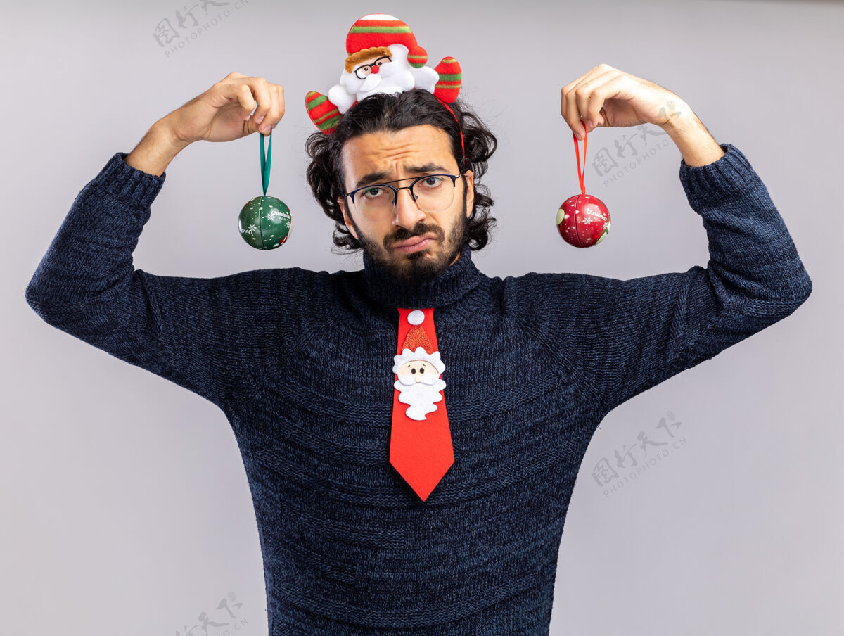 圣诞节悲伤的年轻帅哥戴着圣诞领带 戴着发箍 手里拿着圣诞球 背景是白色的帅哥悲伤头发