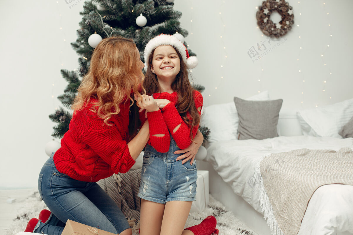节日人们在为圣诞节做准备母亲在和女儿玩耍一家人在节日的房间里休息孩子穿着红色毛衣杉木盒子装饰