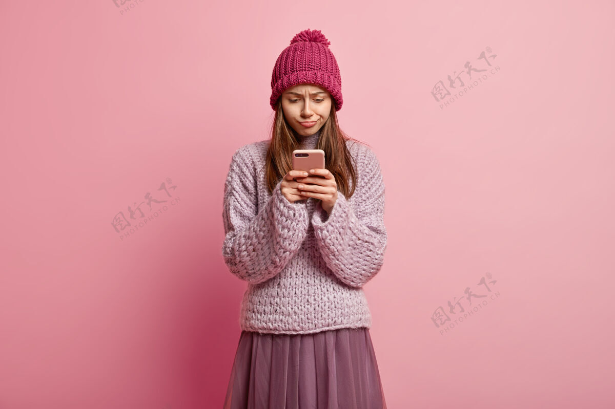 帽子迷茫失意的女模特专注于手机 看陌生短信 上网 穿时髦冬装手机针织通话