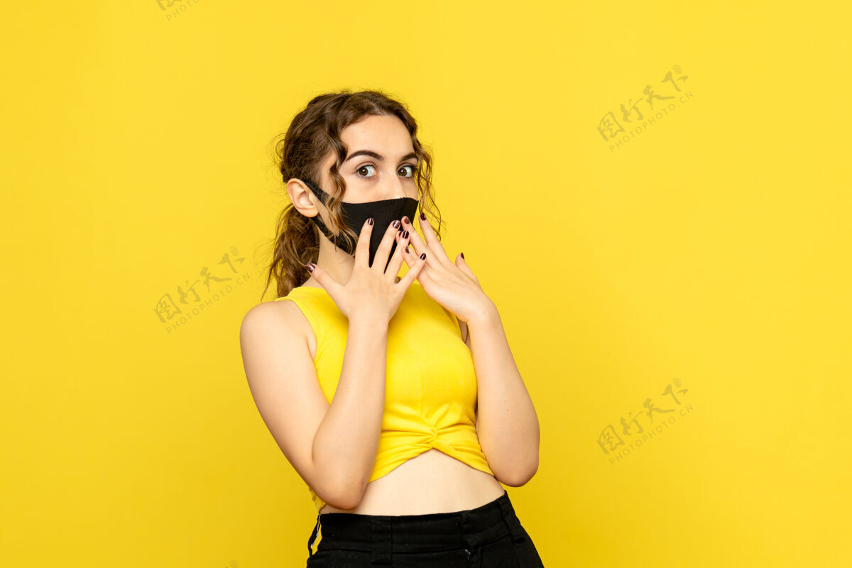 黑发黄墙上戴着黑面具的年轻女子的正视图年轻女性情感可爱