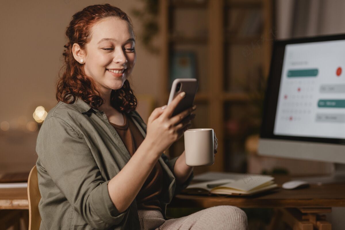 家家里的女人一边喝咖啡一边在电脑前用智能手机杯子当代女人