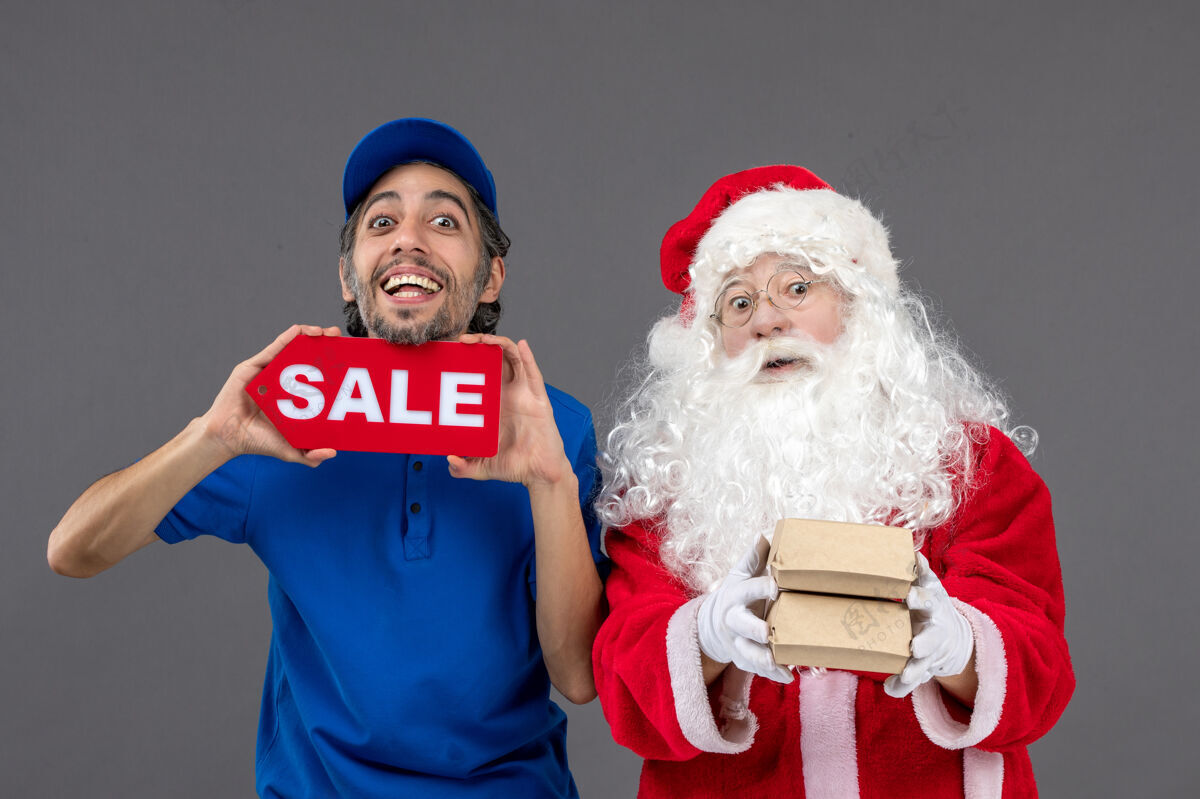 节日圣诞老人的正面图 男性信使手持销售横幅 灰色墙上有食品包装圣诞老人圣诞快乐男性