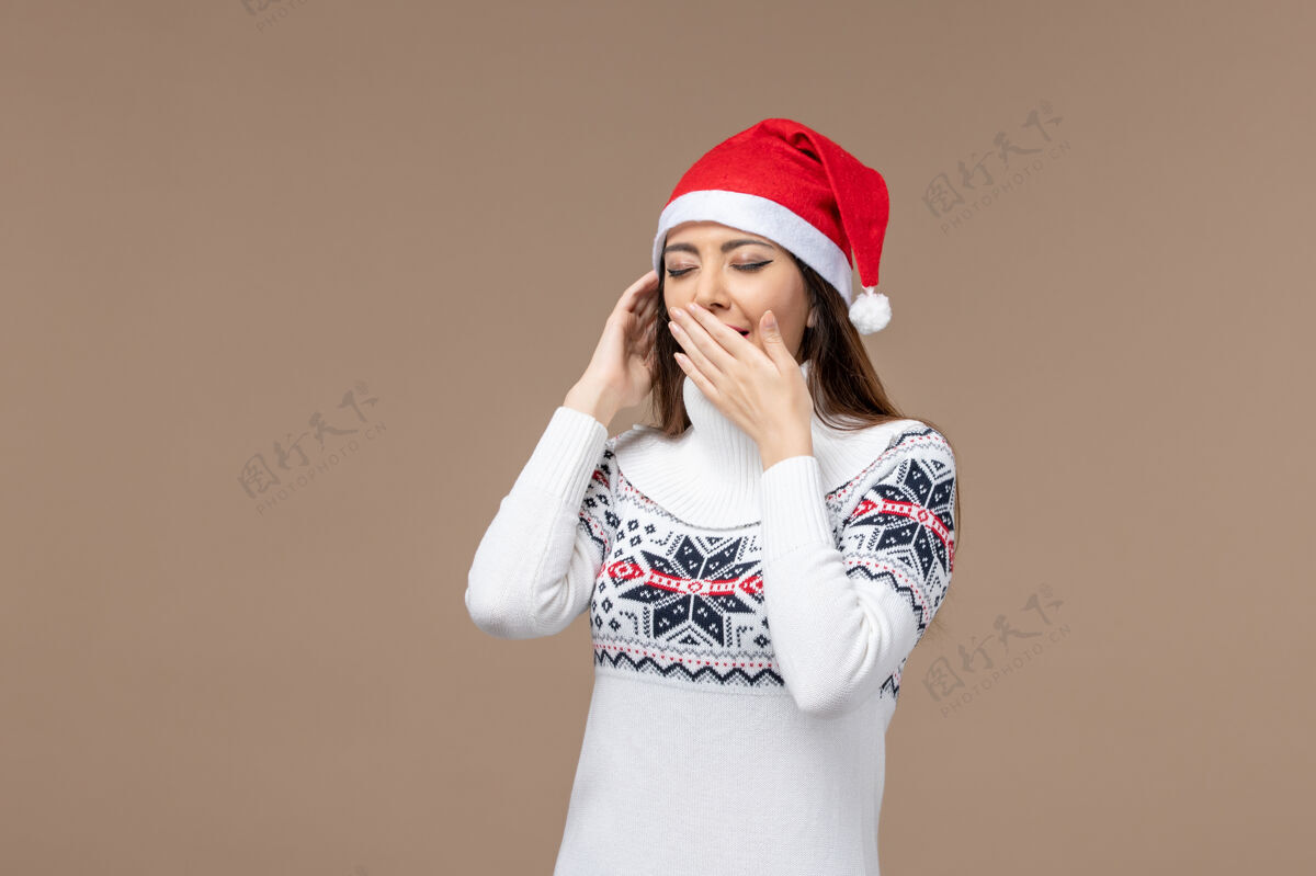 正面正面图：年轻女子在棕色背景上打呵欠 圣诞感慨新年人物肖像摆姿势