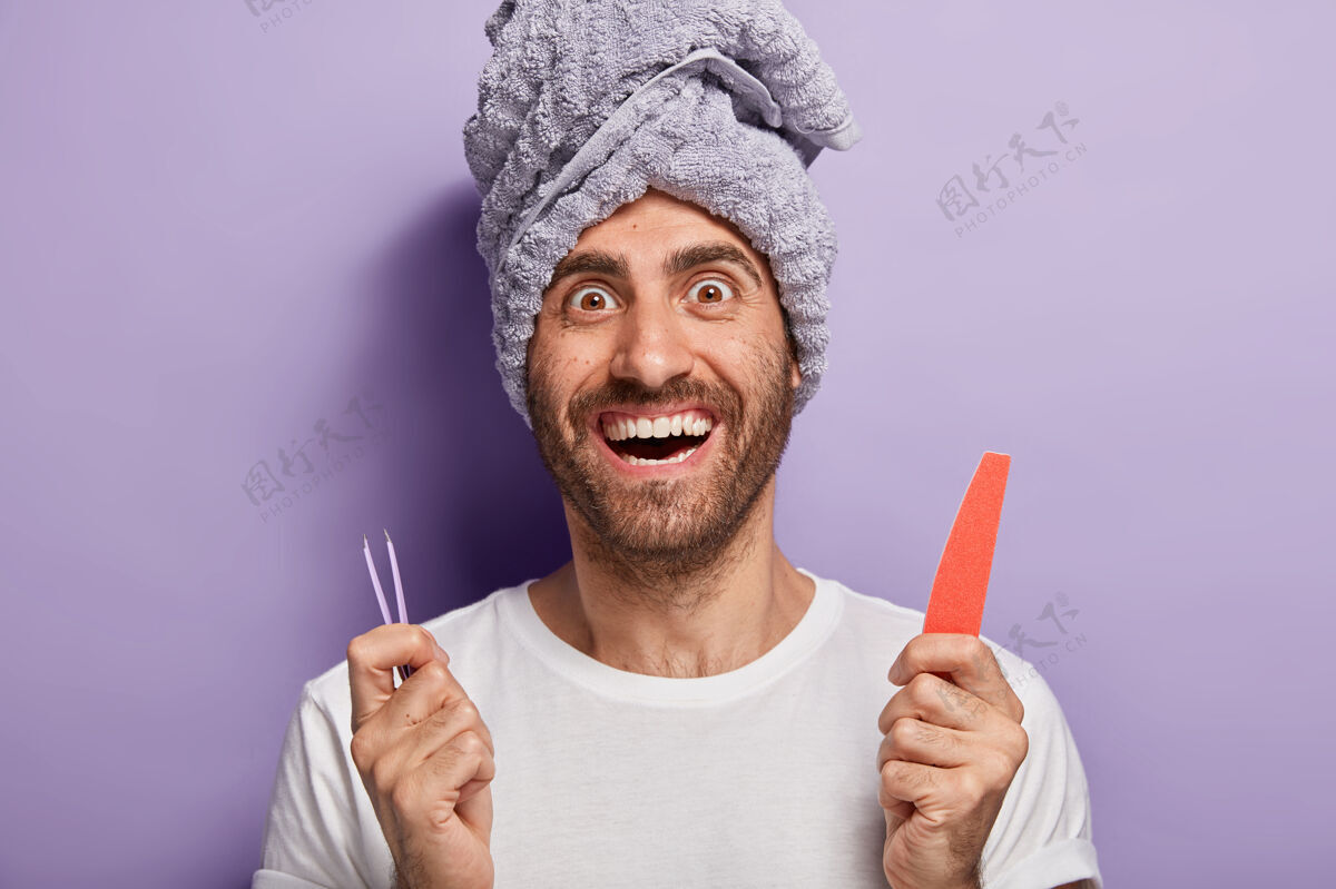 治疗快乐的男人拿着指甲锉和镊子 去美容院或家里做美容 做指甲矫正 头上有毛巾spa镊子Spa惊讶