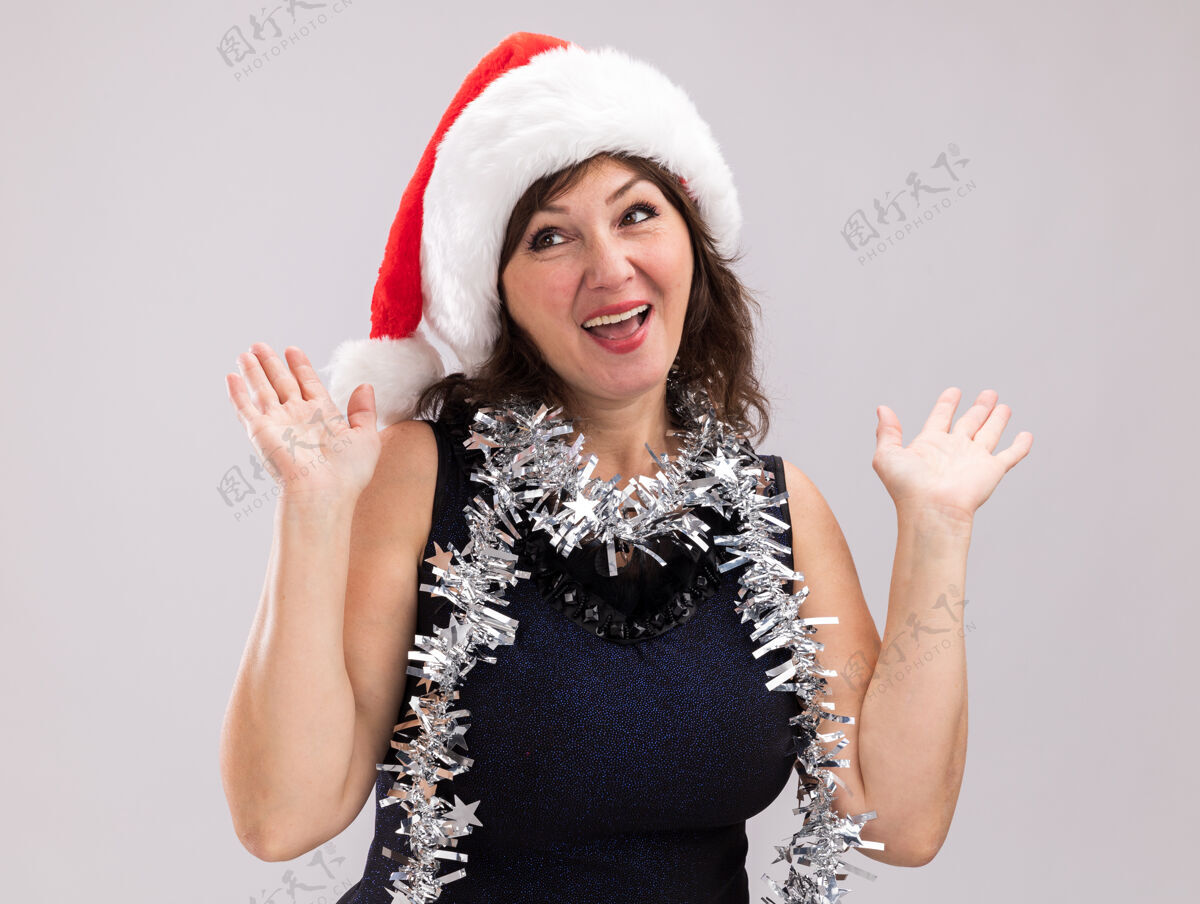 中年一位戴着圣诞老人帽 脖子上戴着金属丝花环的中年妇女看着镜头 在白色背景下 她空手而归脖子帽子金属片