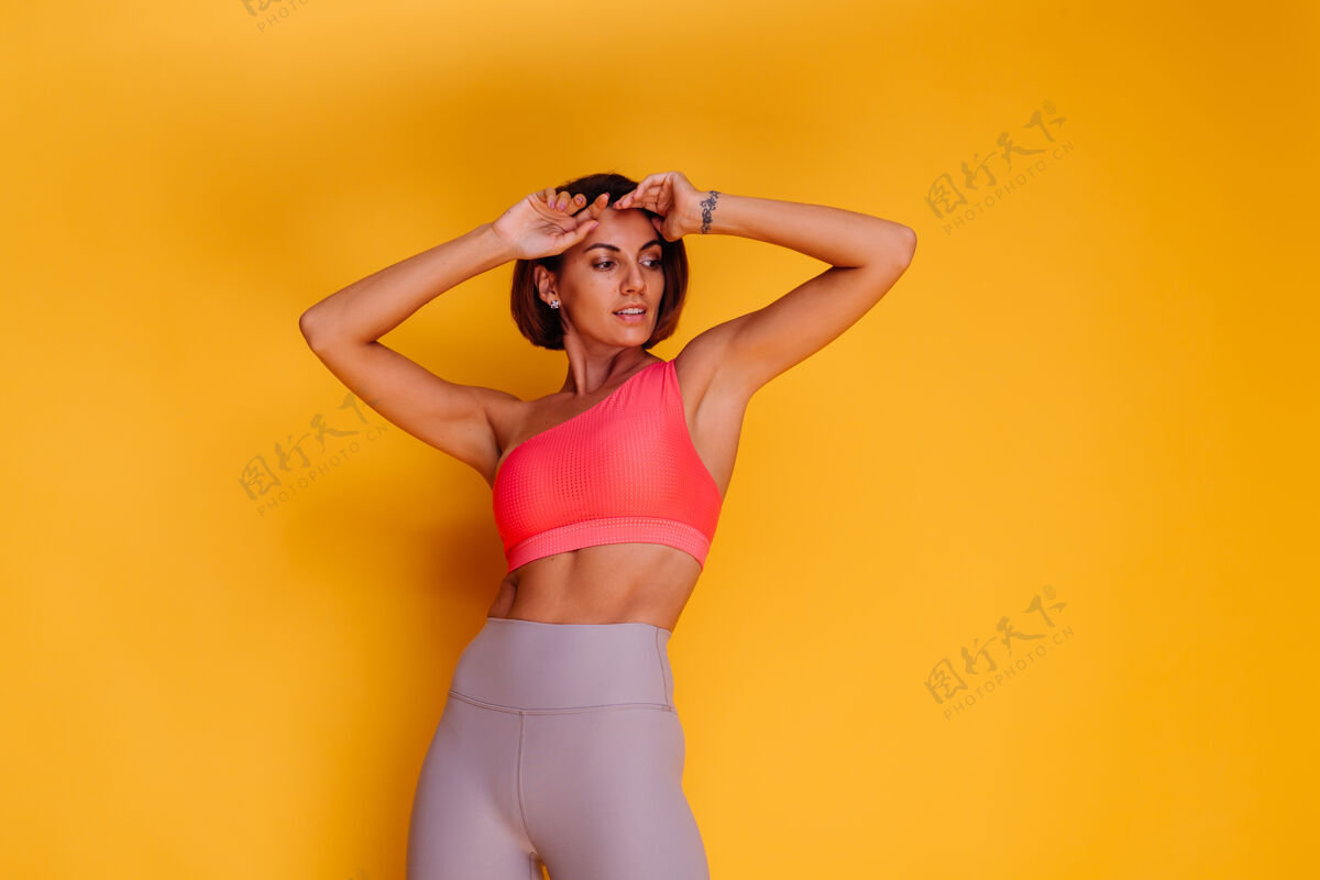 健康年轻健壮的女人穿着运动服 时髦的上衣和紧身裤 对着黄色的墙壁摆姿势人活跃积极