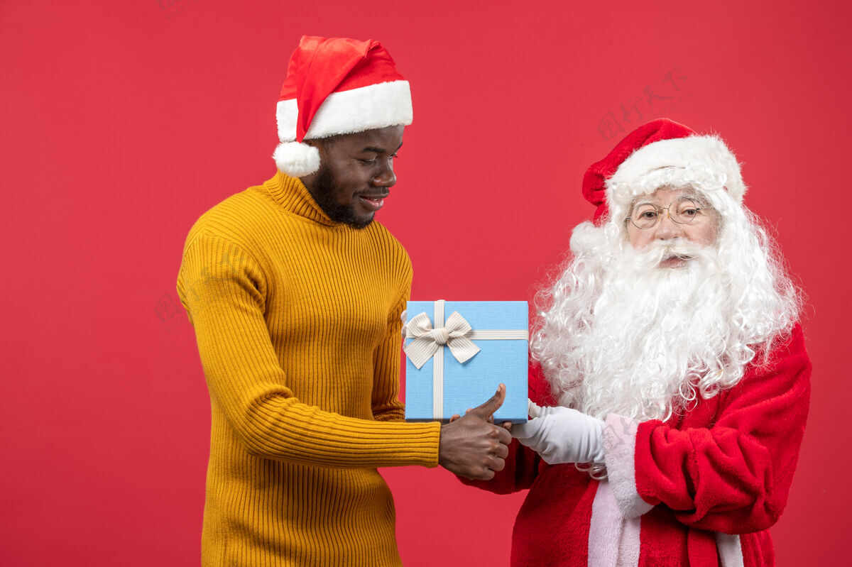 人红墙上的圣诞老人和拿着礼物的年轻人的正视图前面圣诞老人老年