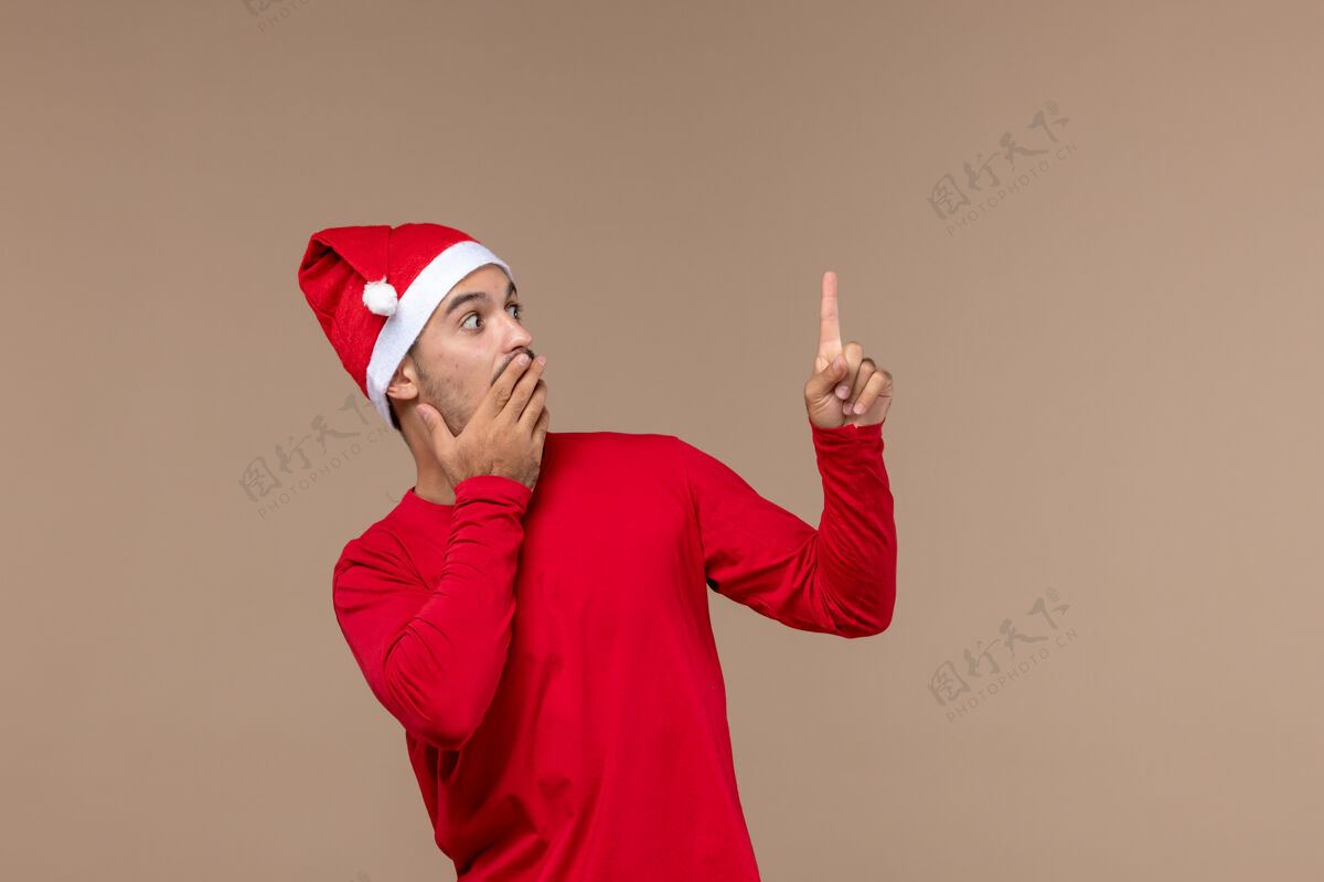 快乐正面图棕色背景上表情惊讶的年轻男性圣诞情感节日男性快乐人棕色