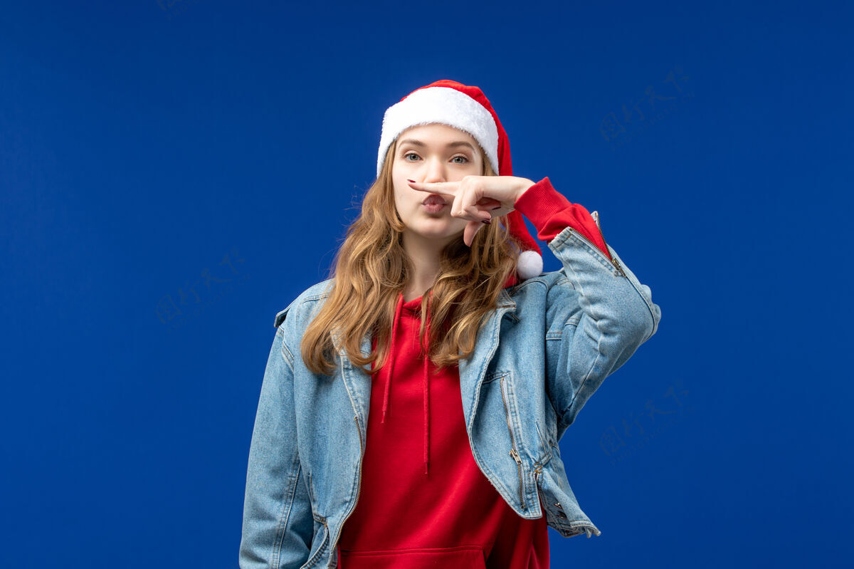 艺人正面图：戴着红色圣诞帽的年轻女性在蓝色背景上摆出圣诞情感色彩音乐家年轻女性颜色