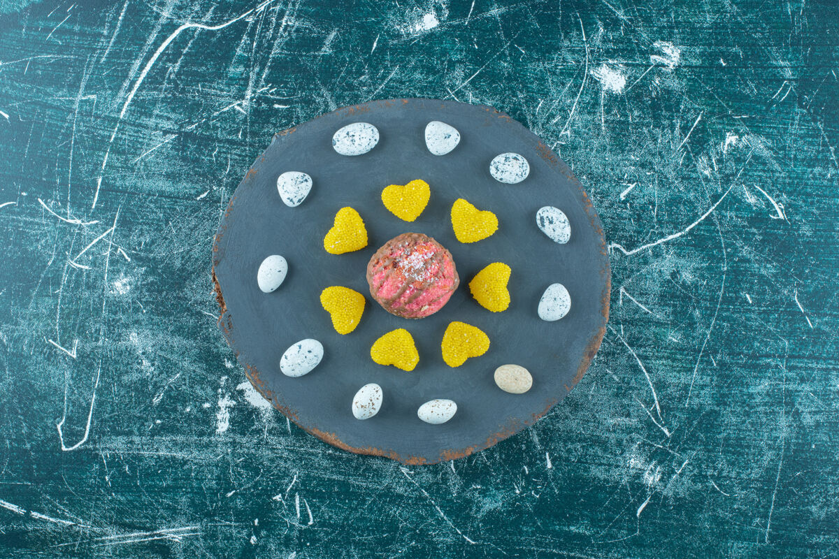 美味在蓝色的木板上 一块涂有巧克力的曲奇周围放着糖果和果酱糖果甜点饼干