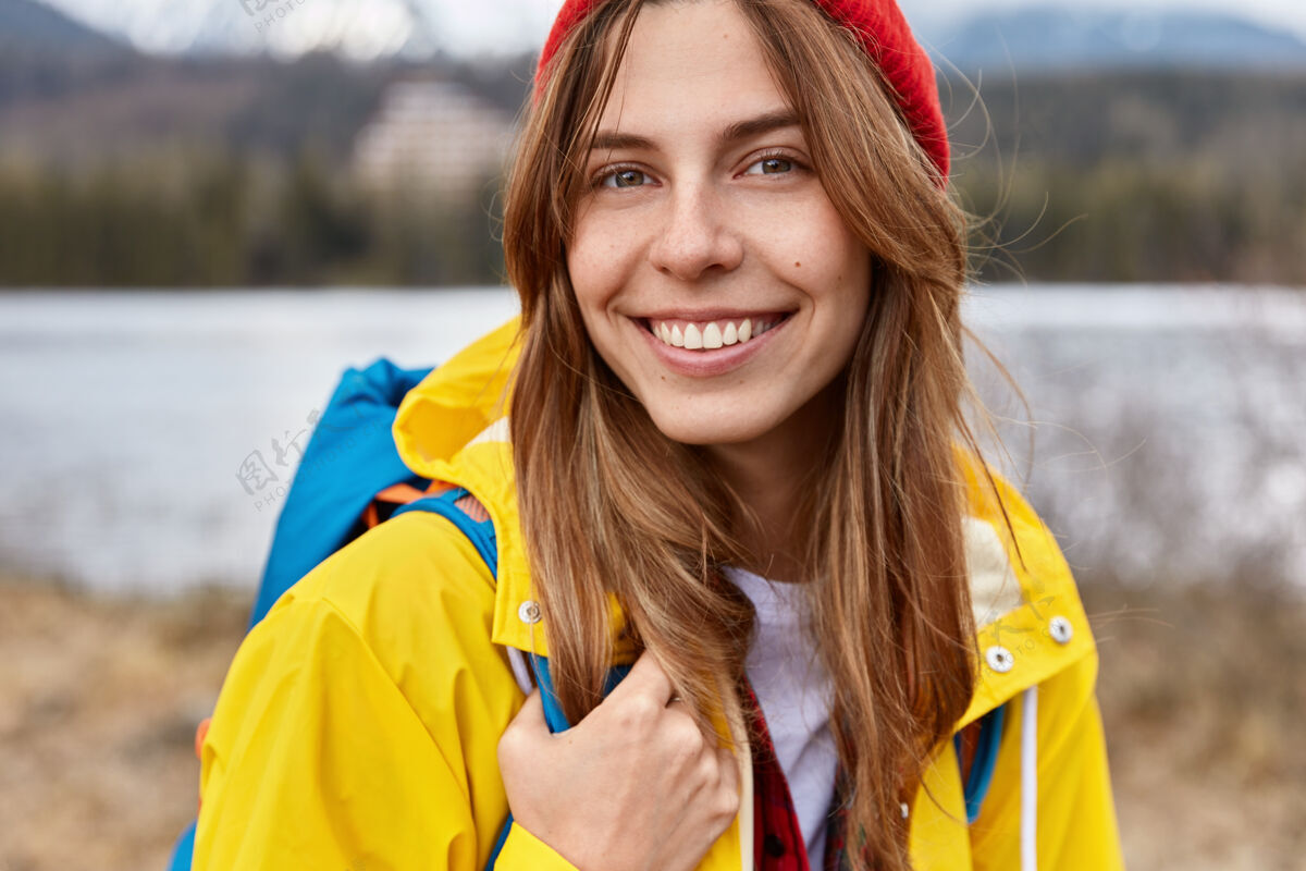 徒步旅行可爱开朗的欧洲女人的剪短形象有着宽大温柔的微笑 长长的直发 戴着红帽子河流积极人类