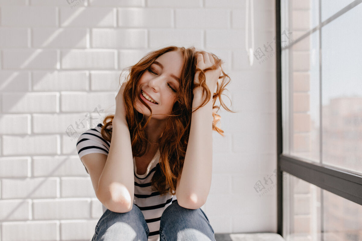 寒冷可爱的白人女孩闭着眼睛微笑温文尔雅的姜女年轻人坐在砖墙上休闲女士阁楼