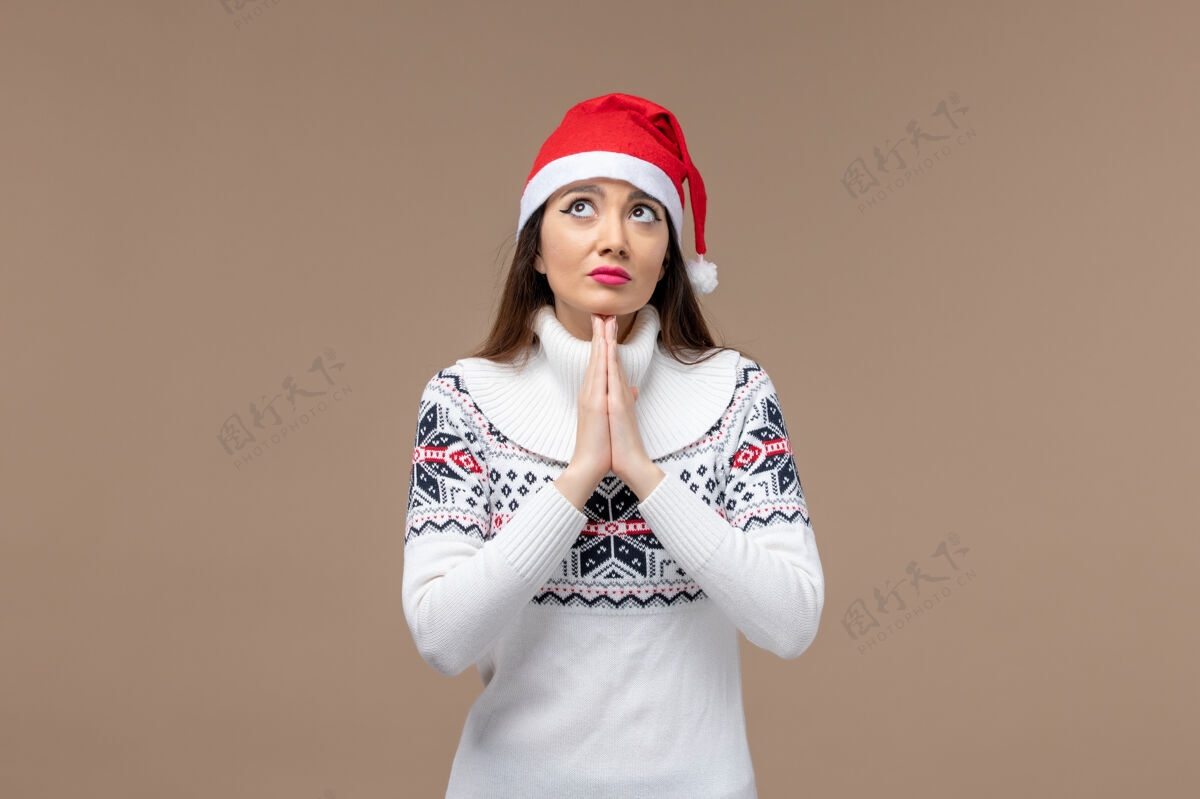 背景正面图：年轻女子在棕色背景上带着祈祷的表情圣诞感慨新年快乐情感微笑
