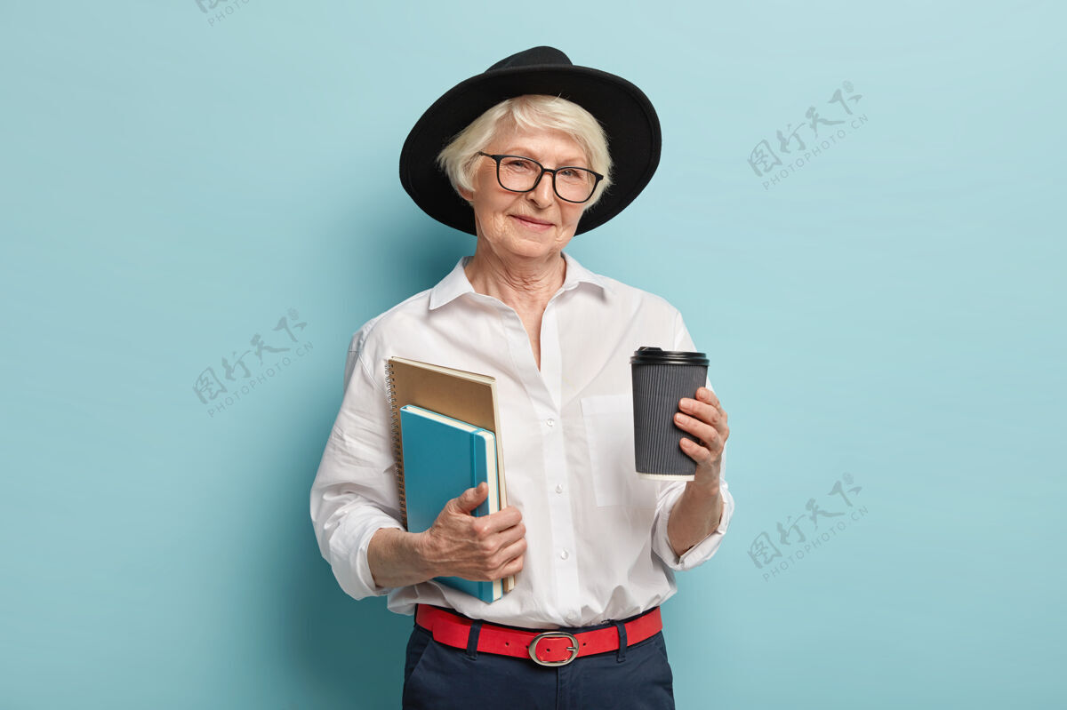 老人晚年读书满脸皱纹 戴着黑头巾 拿着两个笔记本 外卖咖啡 准备讲课 隔着蓝色的墙人 养老 喝酒的概念快乐帽子老人