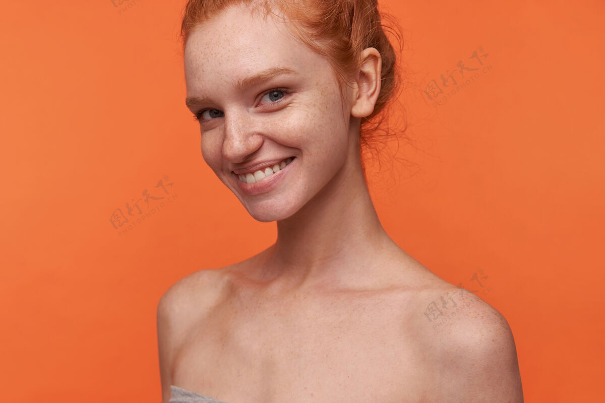 漂亮室内照片：可爱的年轻女士 洁白完美的牙齿 打着蝴蝶结 站在橙色的背景上 双手放在地上 在得到愉快的赞美之后 展现出积极的情绪发型休闲情绪