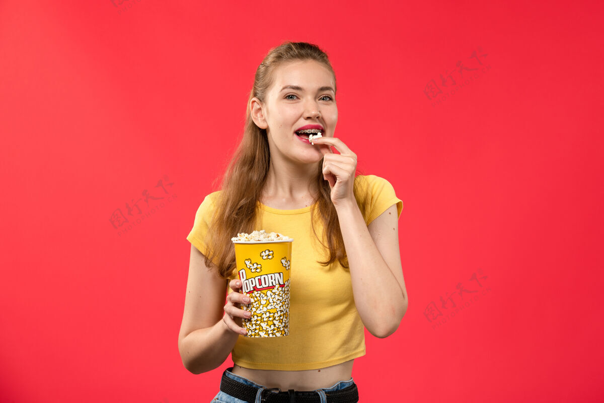 漂亮正面图年轻女子在电影院拿着爆米花吃着红墙电影院里的女性色彩电影年轻人肖像