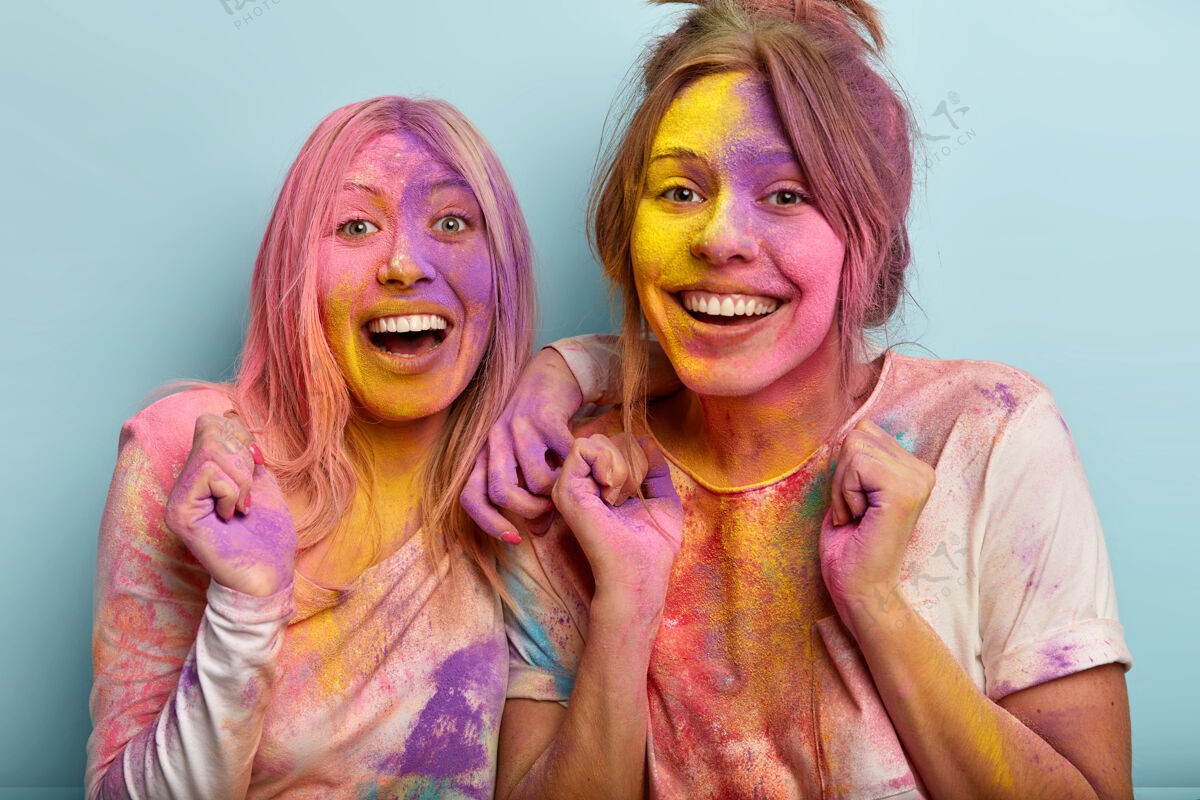 节日快乐快乐的女模特们握紧拳头 享受着油漆庆典 欢笑着 露出洁白的牙齿 涂着彩粉 隔着蓝色的墙壁快乐的胡里节庆典印度教女人颜色