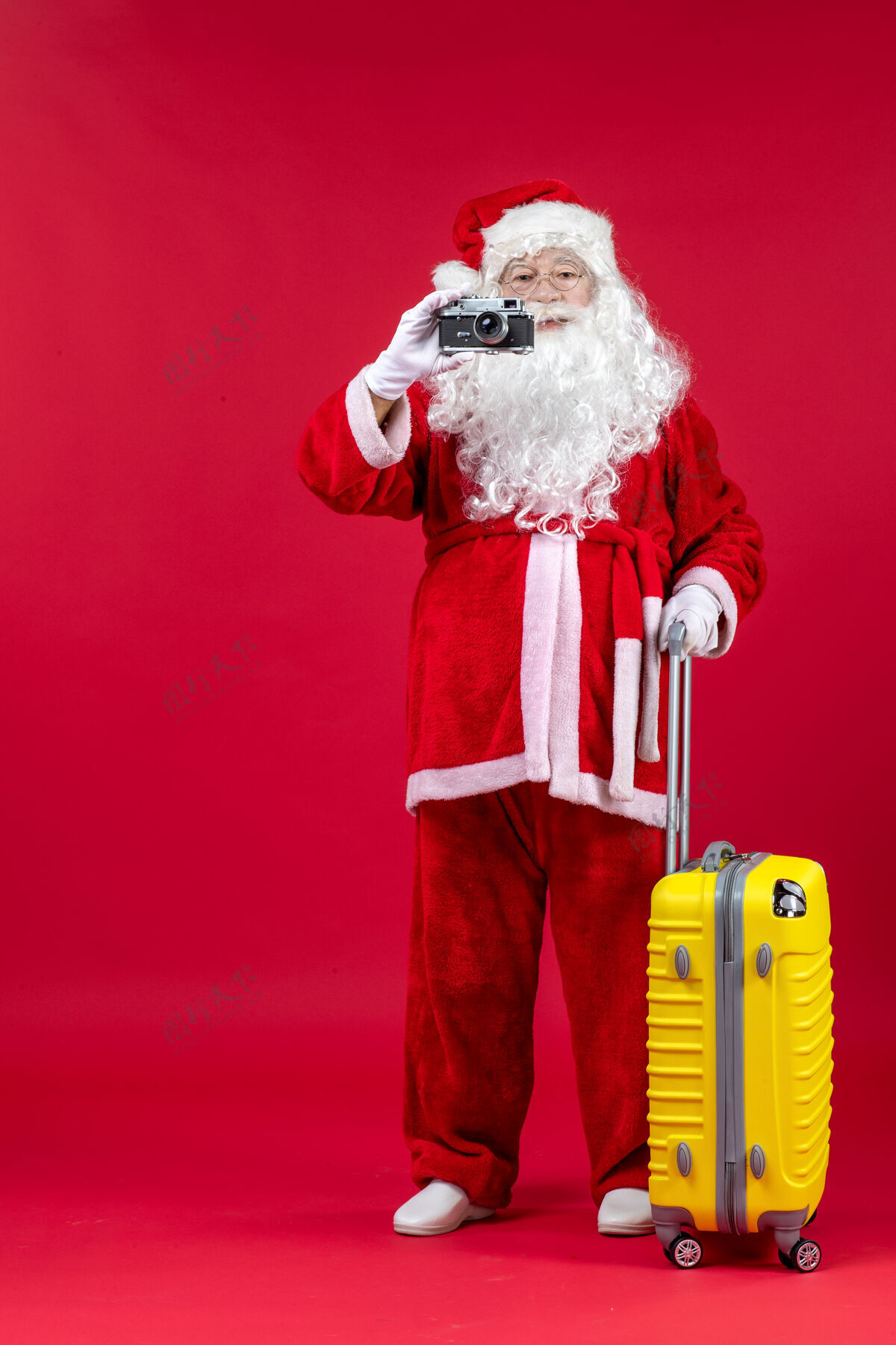 举行红墙上拿着相机的黄色袋子的圣诞老人的正视图圣诞快乐假期服装