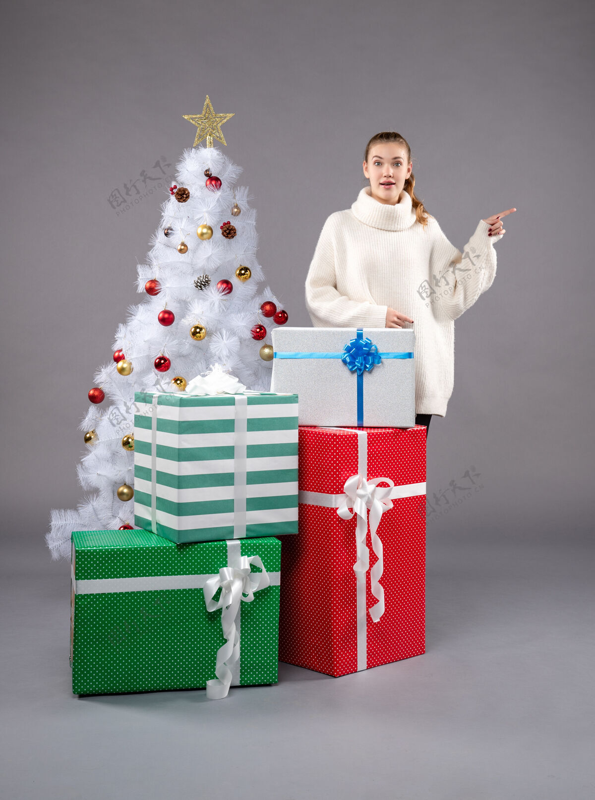 举行年轻的女性在灰色的圣诞礼物周围购物礼物衣服