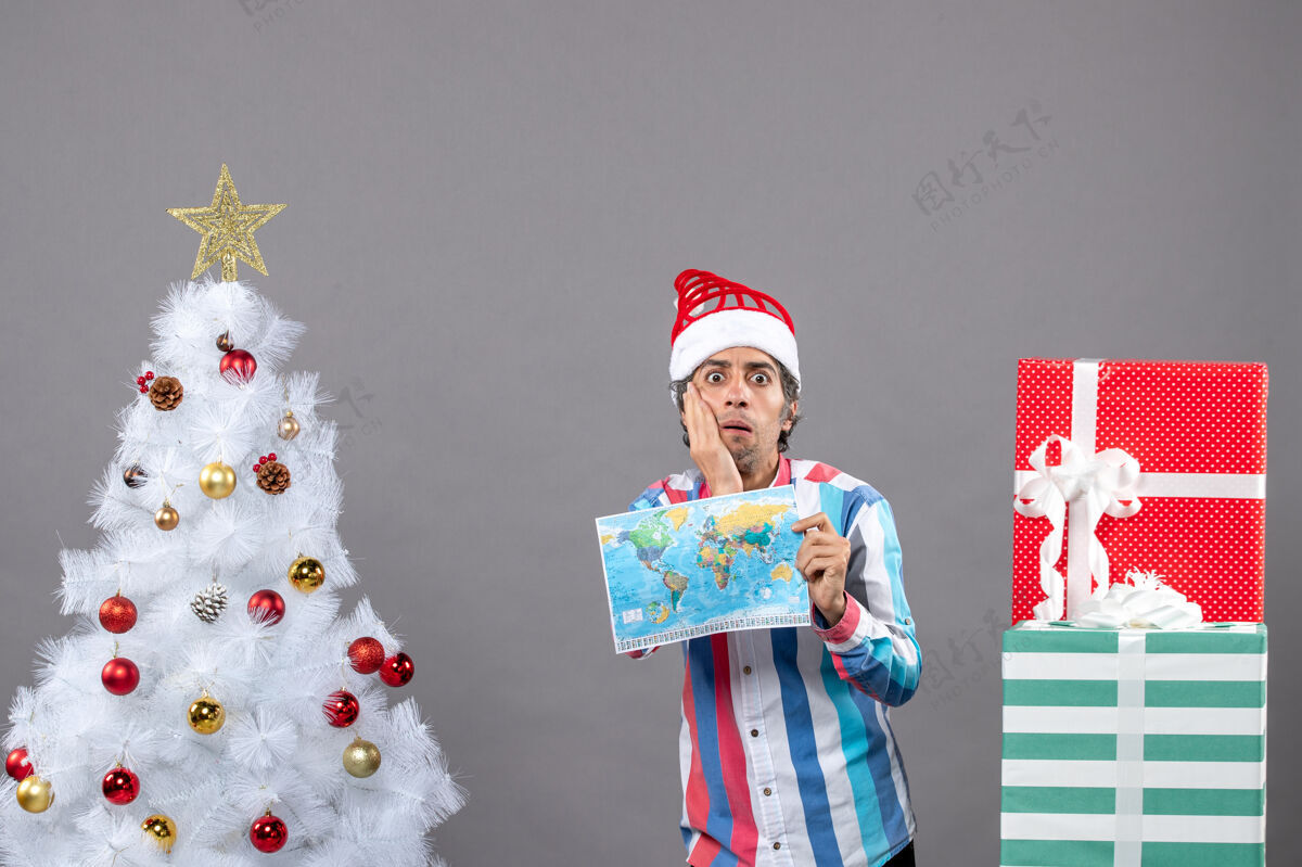 春天前视图惊讶的男子拿着螺旋弹簧圣诞帽拿着世界地图把手放在脸上圣诞老人惊讶的男人抱着