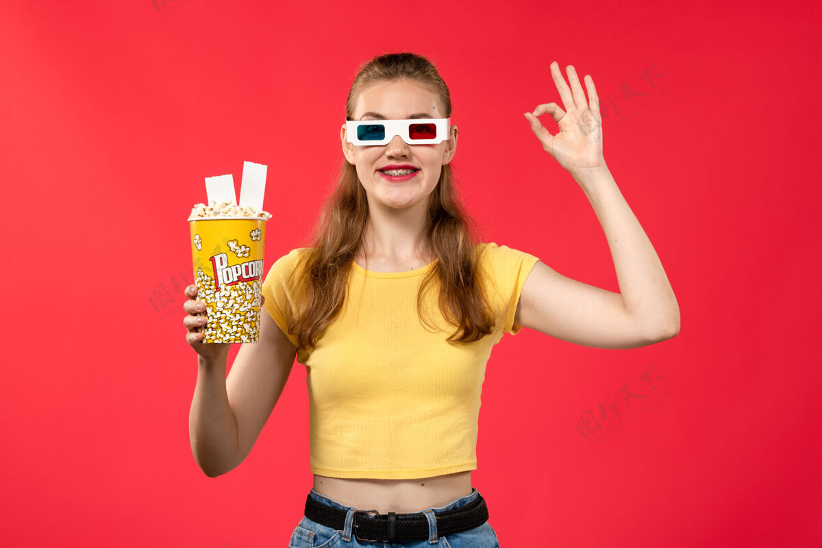 灯光正面图年轻女性手持爆米花包在淡红墙电影院的女孩电影电影包装爆米花