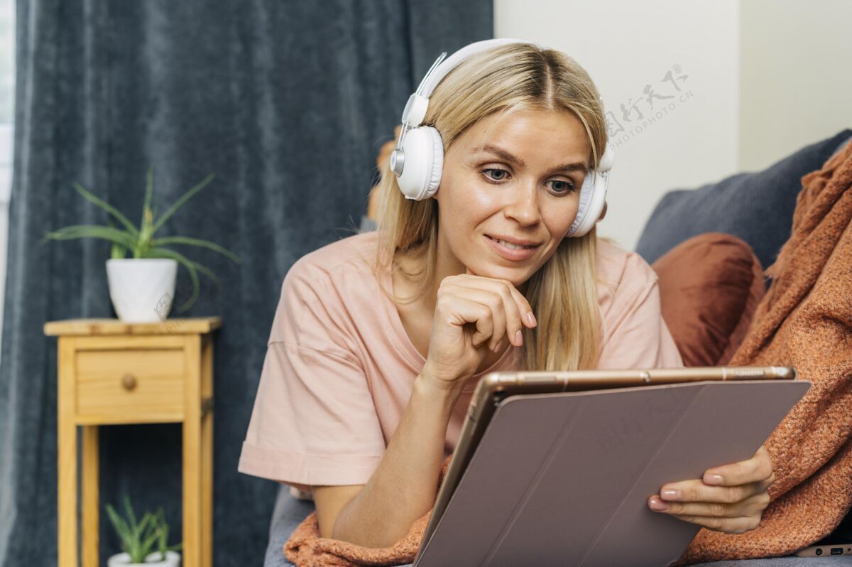 隔离坐在沙发上使用带耳机的平板电脑的女人的正面视图女性耳机流行病