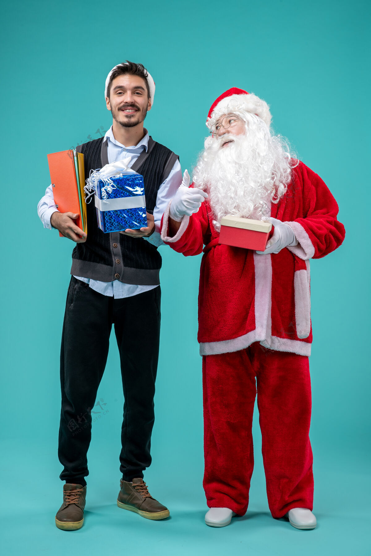 假期圣诞老人与年轻人和礼物在蓝色墙上的正面视图服装节日圣诞老人
