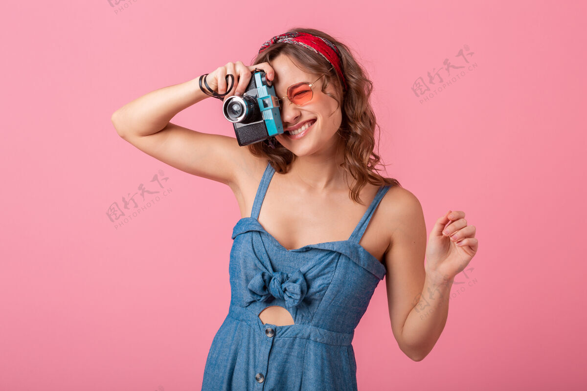 女人迷人的微笑女人在老式相机上拍照 手指向上 穿着牛仔裙 戴着粉色背景的太阳镜微笑相机漂亮